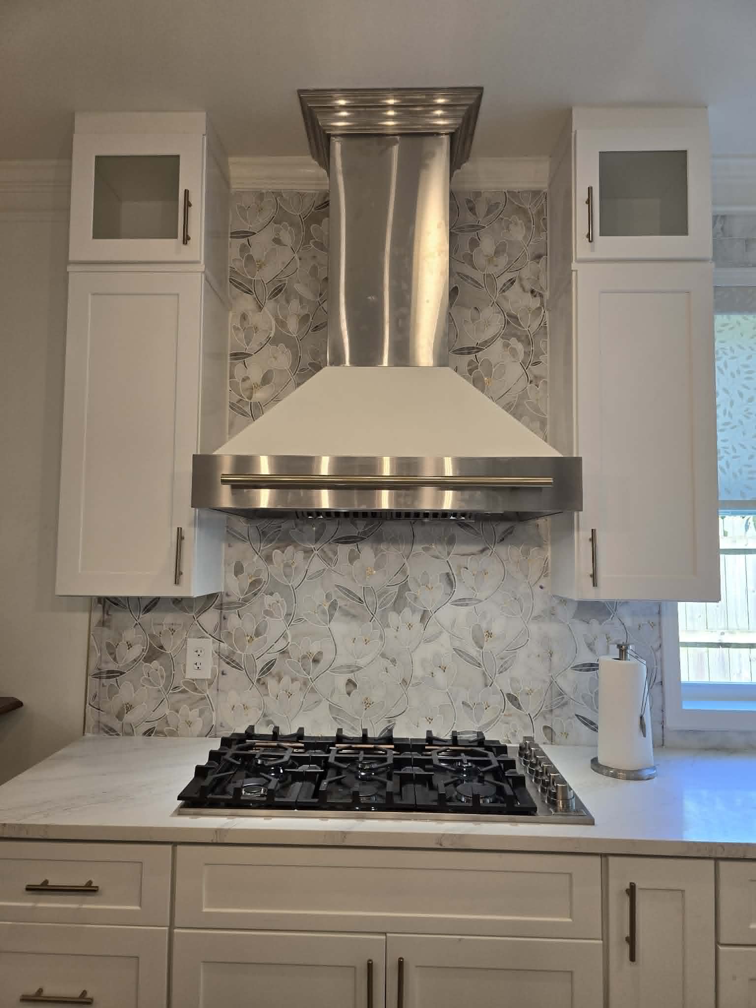 Stainless range hood with floral mosaic tile backsplash